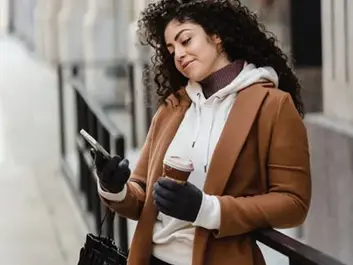 A woman standing in the outdoors with some coffee